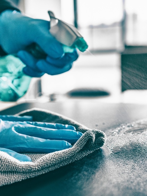 A person with gloves cleaning a table using A wipe and a sanitizer